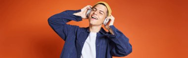 banner of young man pleasure listening to music with headphones against terracotta background clipart