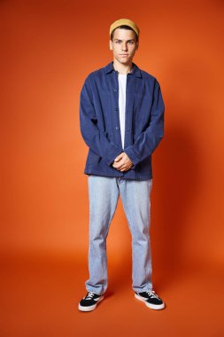 Şık giyinmiş, sarı şapkalı çekici bir genç adam terasotta arka planında duruyor.