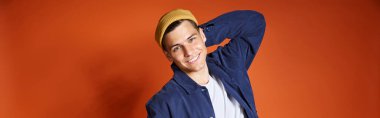 horizontal shot of young man in stylish outfit and yellow hat posing putting hand behind back clipart