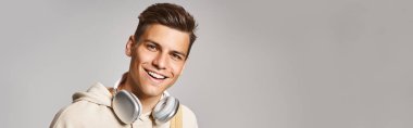 banner of young student in headphones and casual outfit with backpack against grey background clipart