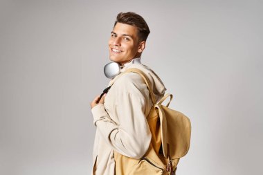 smiling student in headphones and casual outfit with backpack looking from behind back clipart