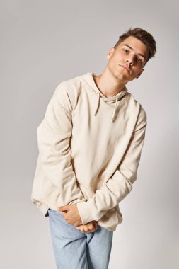 20 'li yaşlarda, kahverengi saçlı, gri gözlü, açık arkaplanda katlanmış ellere poz veren yakışıklı bir adam.