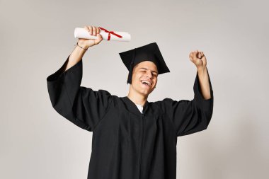 happy young student in graduate outfit happy to have completed his studies on grey background clipart