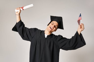 American student in graduate outfit happy to have completed his studies on grey background clipart
