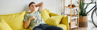 banner of tired young man putting hand behind head and leaning on yellow couch with glasses clipart