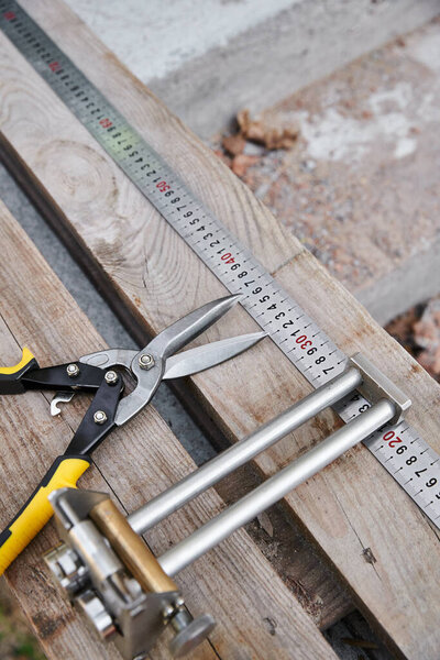 object photo of new metal pliers lying next to measuring tape on wooden table outside of site