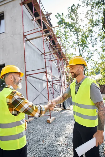 stock image cheerful construction workers shaking their hands and smiling at each other, cottage builders