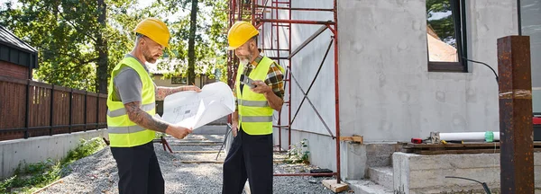 Güzel görünümlü kulübe inşaatçıları inşaat alanı ve afiş düzeyi için planlar üzerinde sıkı çalışıyorlar.