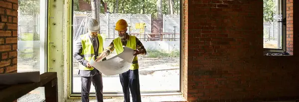 stock image handsome cottage builder and architect with safety gear working with blueprint on site, banner