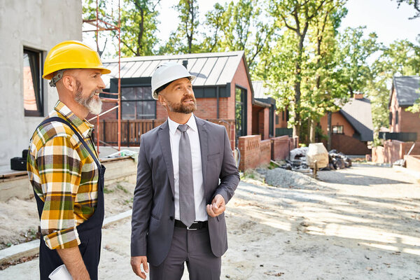 merry cottage builder and architect in suit and overalls with blueprint discussing construction