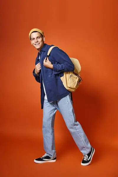 stock image happy man in his 20s with grey eyes and backpack walking on terracotta background