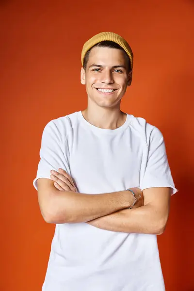 stock image portrait of attractive young man in white t-shirt and yellow hat smiling with arms crossed