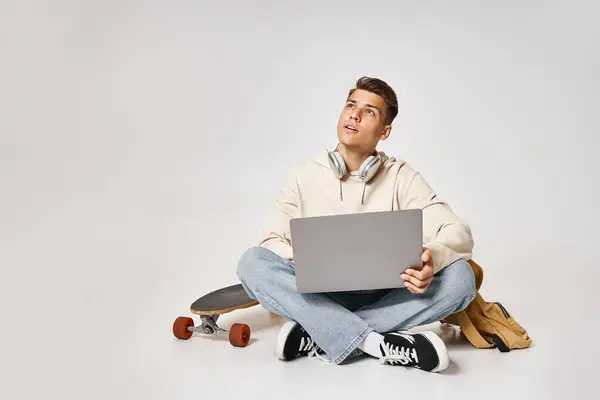stock image handsome student in headphones networking to laptop and sitting with backpack and skateboard