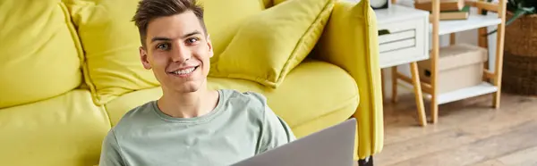 stock image banner of student on floor near yellow couch at home sitting with laptop and smiling to camera