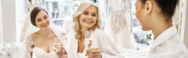 A young bride in a wedding dress raises her champagne flute with her two bridesmaids in a bridal salon. clipart