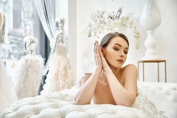 オリジナルの白いベッドの上に平和的に横たわる流れるウェディングドレスの若いブルネットの花嫁 — ストック写真