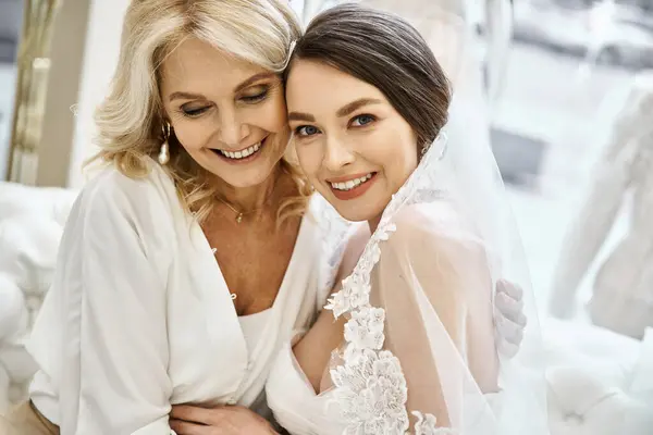 一个穿着婚纱的年轻的黑发新娘和她中年的金发母亲肩并肩站在一家婚纱沙龙里 — 图库照片
