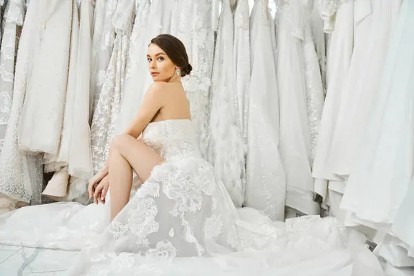 若いブルネットの花嫁がドレスの棚の前に座り 結婚式の日のための完璧なガウンを慎重に選択します — ストック写真