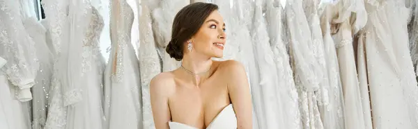 stock image A young, beautiful brunette bride stands among a rack of white wedding dresses in a bridal salon.