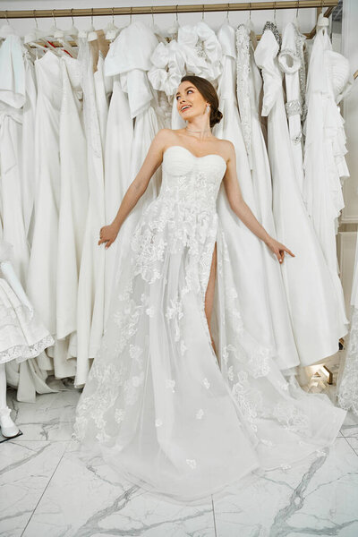 A young, beautiful bride admires a rack of dresses in a wedding salon, contemplating her perfect gown.
