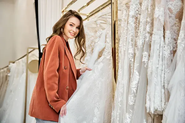 若い美しい花嫁は 慎重に彼女のオプションを調べ ウェディングドレスの棚の前に立っています — ストック写真