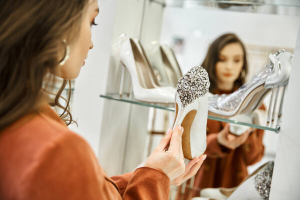 A woman, shopping for her wedding, gazes at her shoes in a mirror with curiosity and excitement.