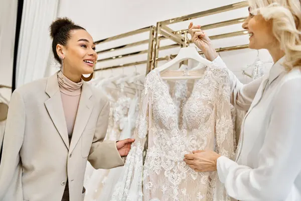 在一名售货员的协助下 年轻女子在婚纱店的衣架上欣赏婚纱 — 图库照片