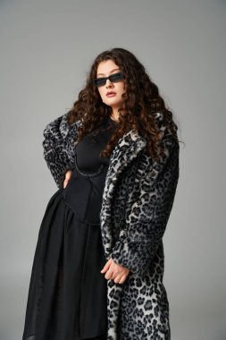 Leopar kürklü, güneş gözlüklü, belinde öne doğru eğilmiş çekici bir kız.