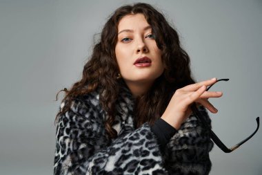 Leopar kürklü çekici bir kadın. Gri arka planda güneş gözlüğü takıyor.