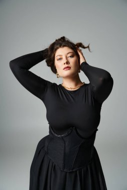 Yirmili yaşlarda çekici bir kız ellerini başının arkasına koyuyor ve gri arka planda saçlarını tutuyor.