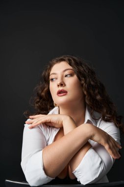 portrait of attractive plus size woman in her 20s hugging neckline and looking to side clipart