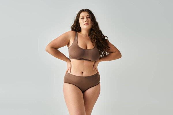 красивая пышная молодая женщина в коричневом нижнем белье с вьющимися волосами, позирующие руки на талии