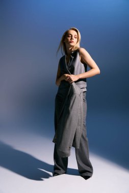 Modaya uygun gümüş takım elbiseli güzel bir kadın koyu mavi arka planda poz veriyor ve başka tarafa bakıyor.