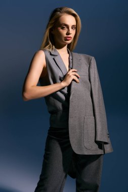 elegant woman in silver chic vest and suit posing on dark blue backdrop and looking at camera clipart