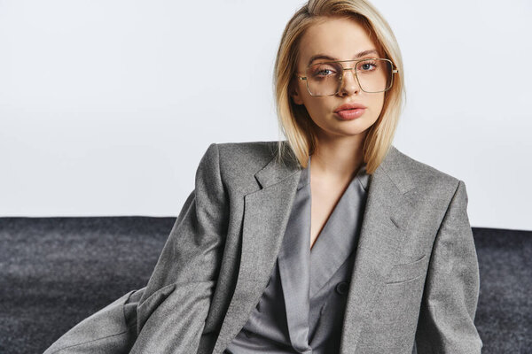 модная шикарная женщина в модных очках в элегантном костюме сидит на полу и смотрит в камеру