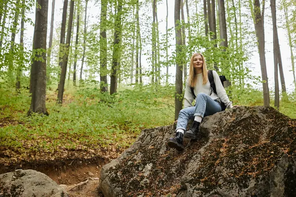 アクティブな若いブロンドの女性ハイカー平和な森でのバックパッキング旅行に岩の上に座って — ストック写真