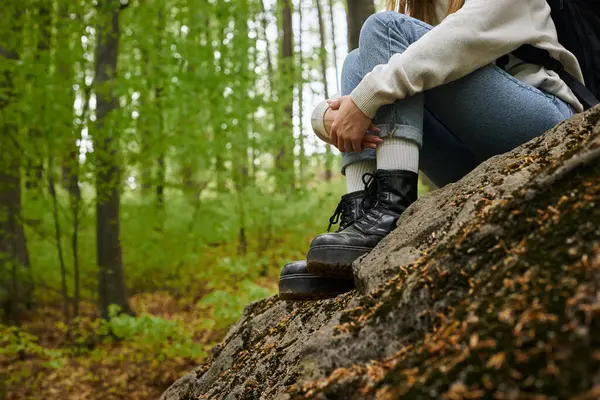 森に座っているジーンズとハイキングブーツを身に着けている彼女の足を抱擁する女性のハイカーのクロップされたイメージ — ストック写真