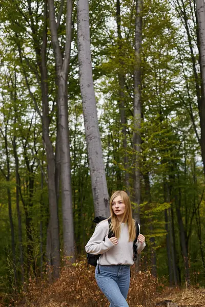 緑の森で熱狂的でブロンドの少女はセーターとジーンズを着て 風光明媚な景色を探索する — ストック写真