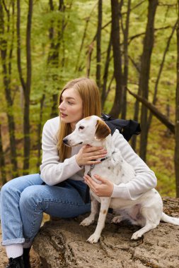 Caring blonde woman hugging her dog, while having a halt on forest trip, both looking away clipart