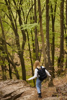 Back view of woman hiker with backpack walking through a forest for adventure backpacking in nature clipart