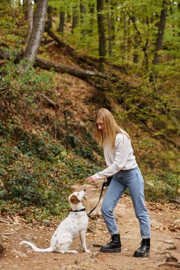 Happy girl interact with her pet holding leash at hiking rest with mountain and forest view clipart