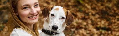 Şirin köpek ormanda güzel sarışın bir kadınla oturuyor. Yürüyüş yaparken kameraya bakıyor.