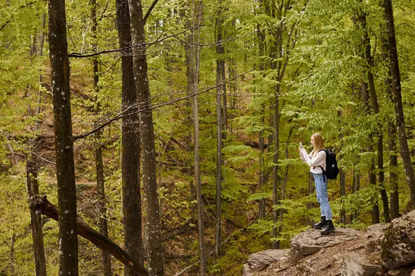 stock image Side view of active blonde woman wearing backpack on hiking and taking photos on phone