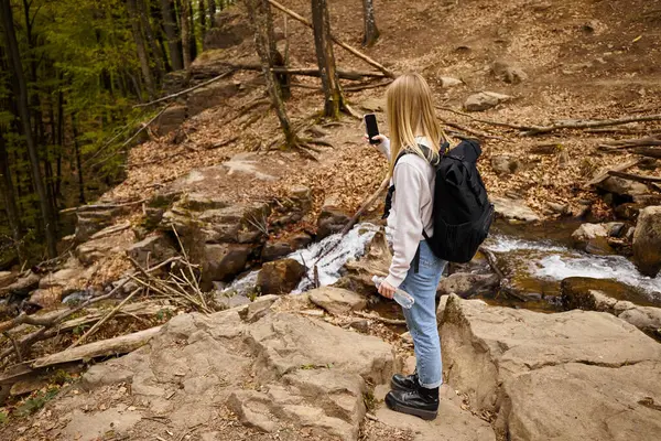 水のボトルを保持している森を渡るセーターとジーンズを身に着けている女性旅行者のバックビュー — ストック写真