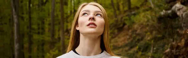 Relaxed blonde woman breathing fresh air in forest on solo hiking trip looking in the sky, banner