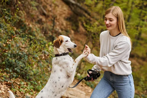 Smiling woman training her pet dog holding leash at hiking halt in deep forest