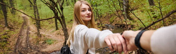 Woman leading way, point of view photo of couple holding hands crossing stream in forest, banner