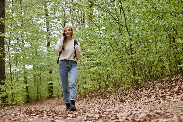 Full length photo of woman traveler with backpack talking by phone walking in forest path