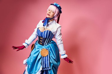 Mavi şapkalı ve canlı giyinmiş, pembe arka planda kameraya bakan çekici bir kadın Cosplayer.