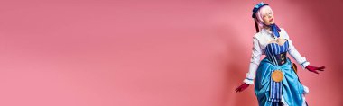 Mavi şapkalı ve canlı giyinmiş seksi bayan Cosplayer pembe arka planda kameraya bakıyor.
